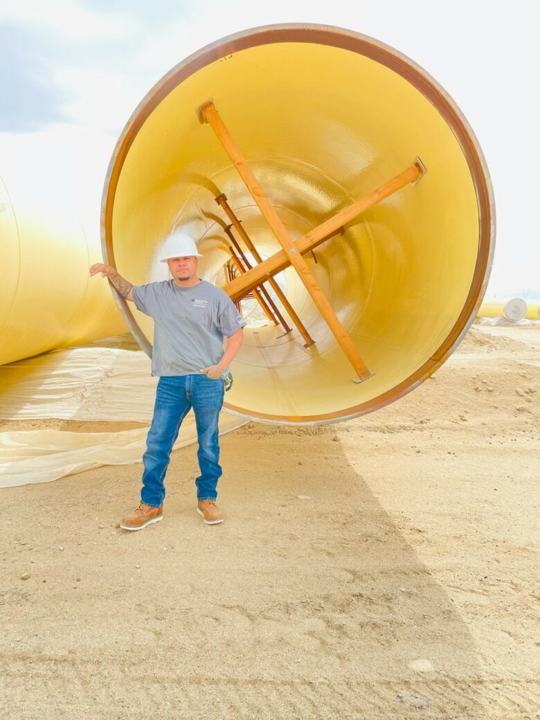 Jose Figueroa in hard hat standing next to Large Diameter Pipe 