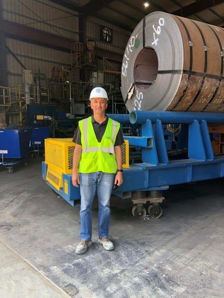 Carlos Garcia in a safety vest and helmet standing in front of a steel coil