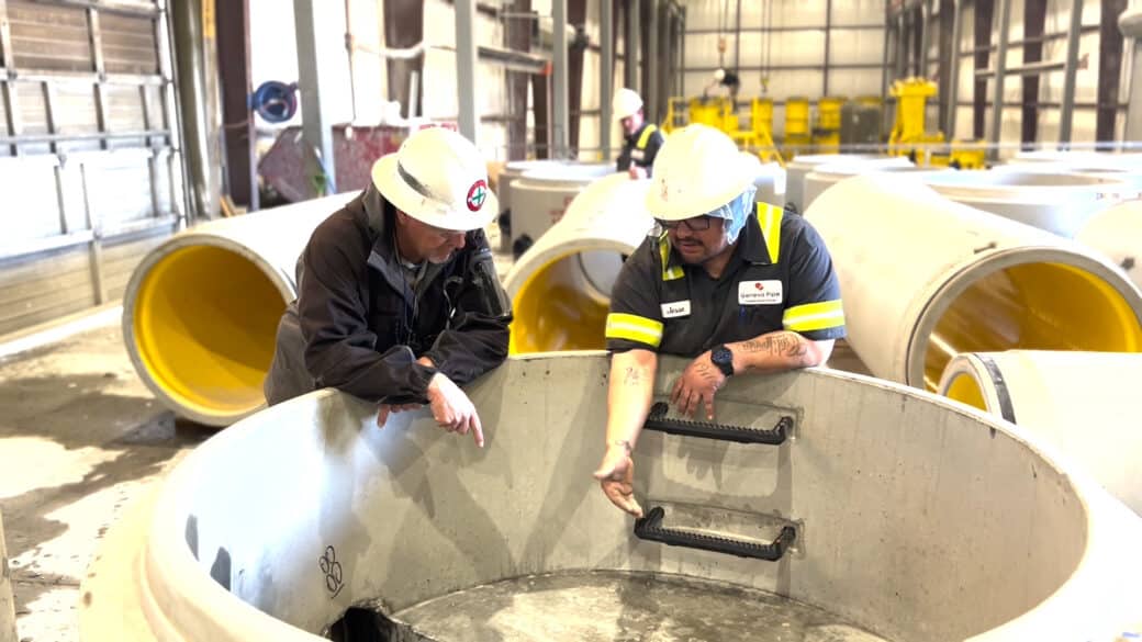 Team members in safety helmets inspect a precast manhole inside the manufacturing plant