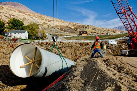 homepage man helping lower large pipe into ground