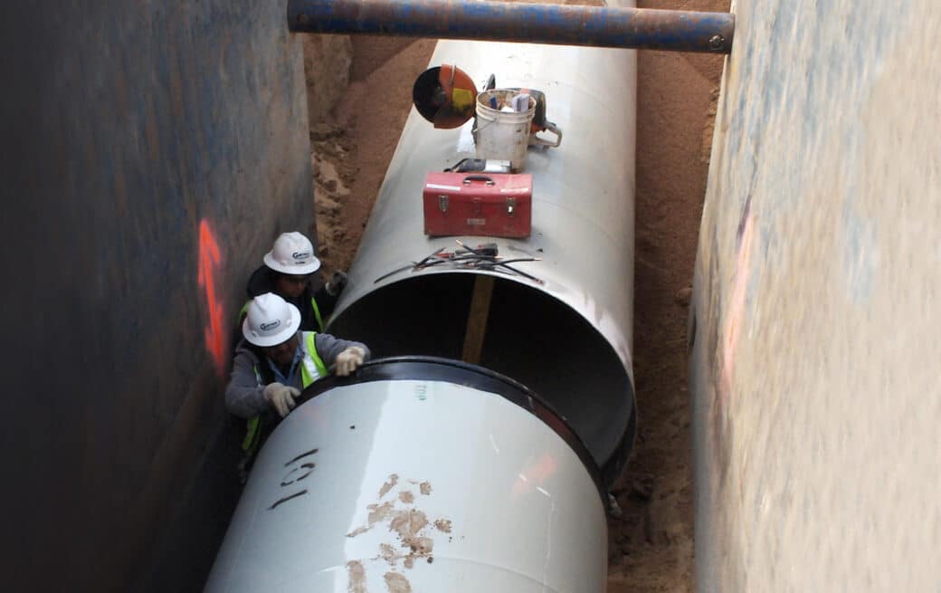 Two workers installing pipe in trench