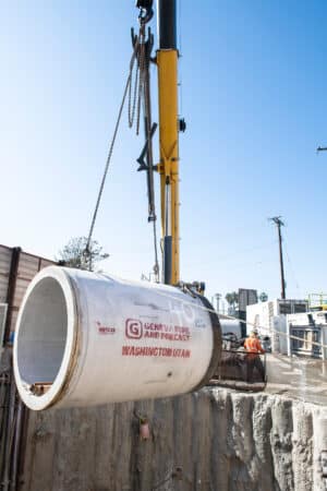 Concrete jacking pipe being lifted by crane into trench