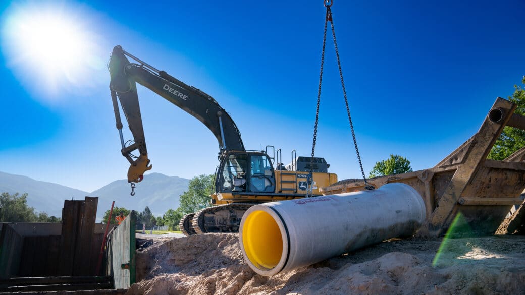 Lined concrete pipe being lifted into trench with crane