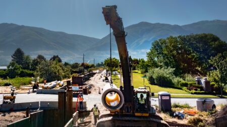 Crane lifting lined RCP to place into trench, street and mountains in background