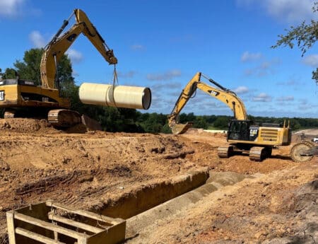 Excavator installing steel pipe into trench