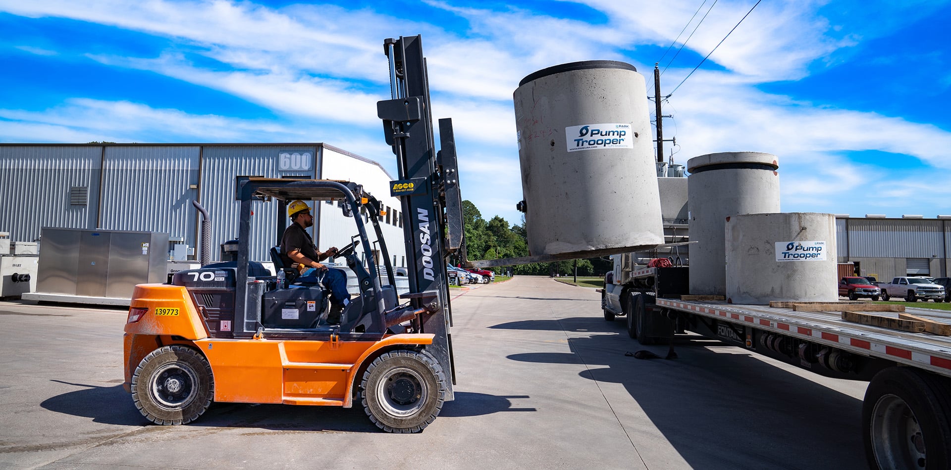orange forklift placing a concrete cylinder onto a truck bed