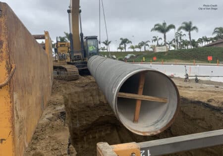 Crane lifting pipe into trench