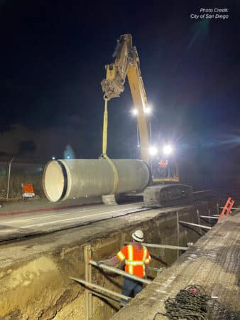 crane lifting pipe into trench, night sky